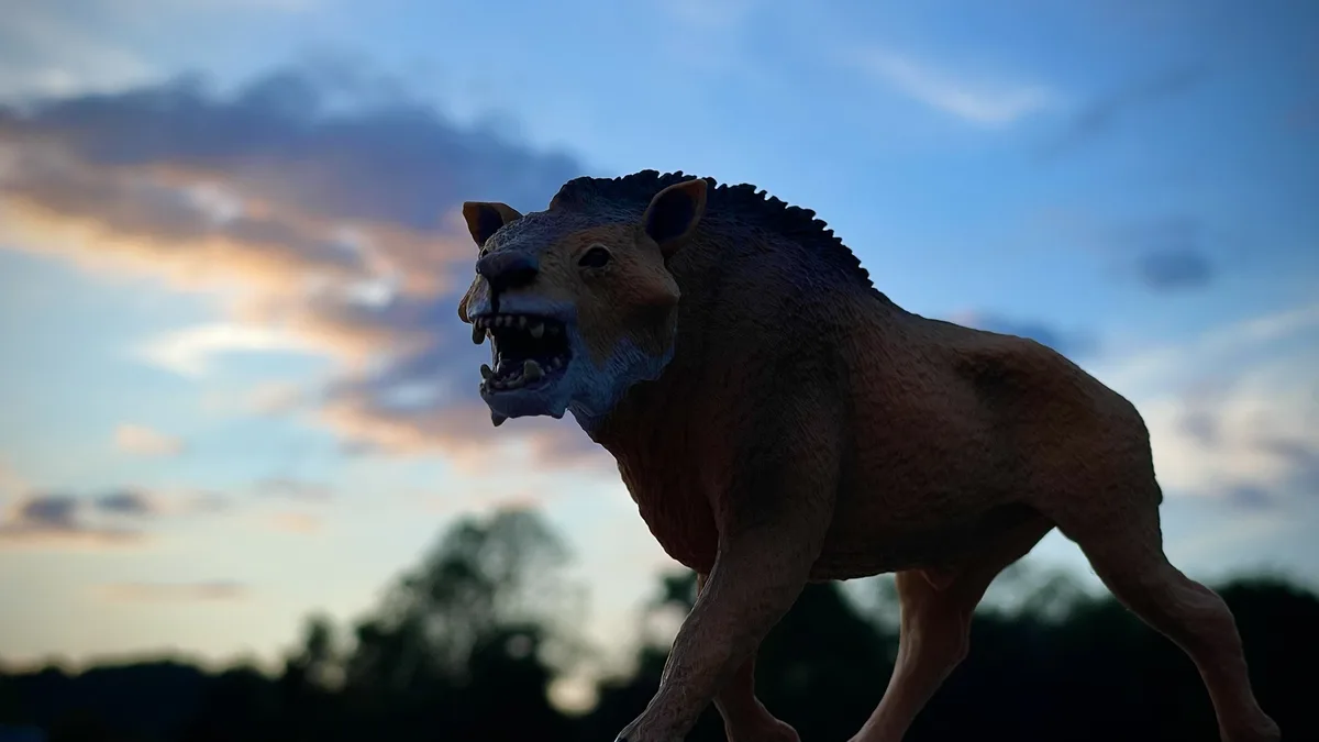 A plastic toy model of a saber-toothed cat or similar prehistoric predator is shown in a menacing pose against a twilight…
