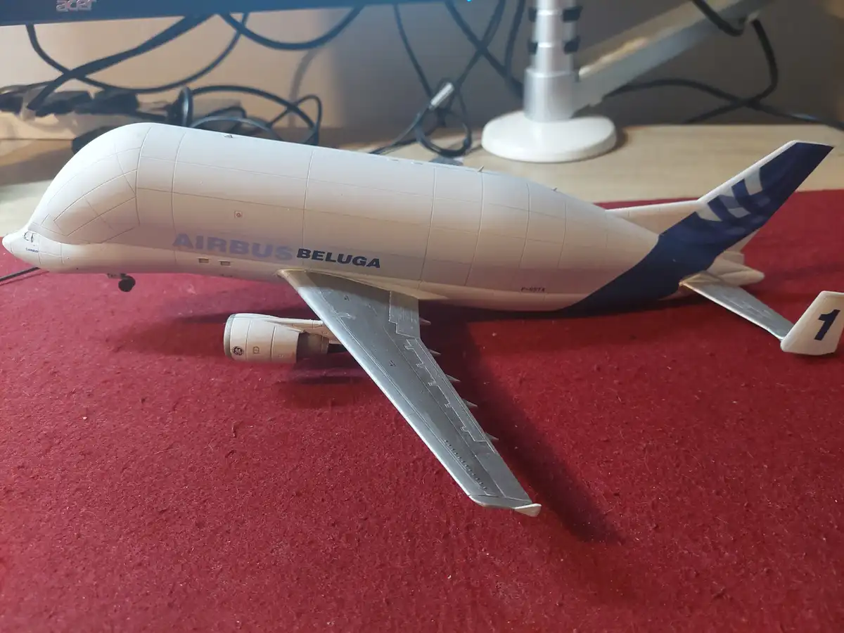 A white model of an Airbus Beluga cargo plane with blue tail markings and the text 'AIRBUS BELUGA' on its side lies on a red…