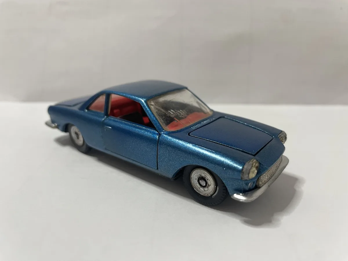 A blue vintage toy car with red interior sits on a plain white surface, its windshield showing a faint reflection. The…