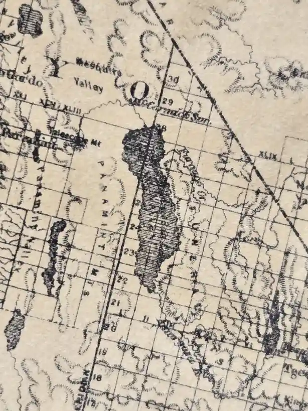 A close-up of an old, sepia-toned topographic map showing a grid of numbered squares and labeled geographical features like…