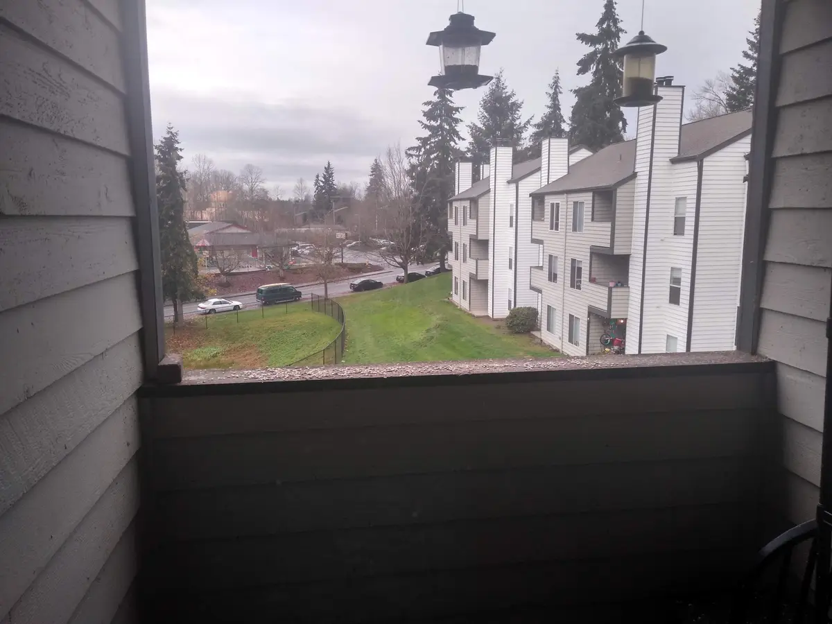 A view from a balcony looking out onto a residential area with apartment buildings, cars, and trees under an overcast sky…