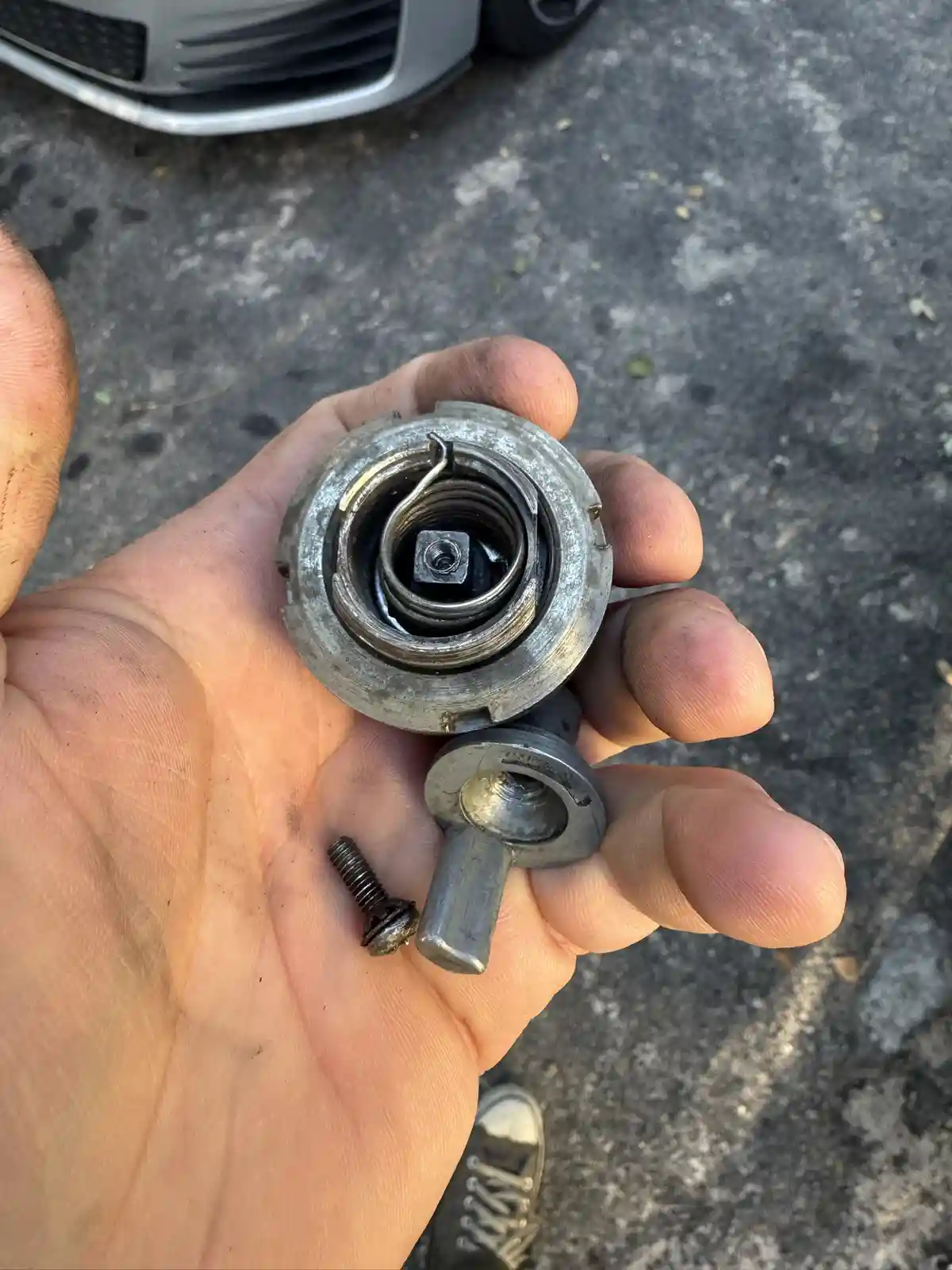 A person holds a disassembled car part, revealing a coiled spring inside a metal housing, with a small bolt and another…