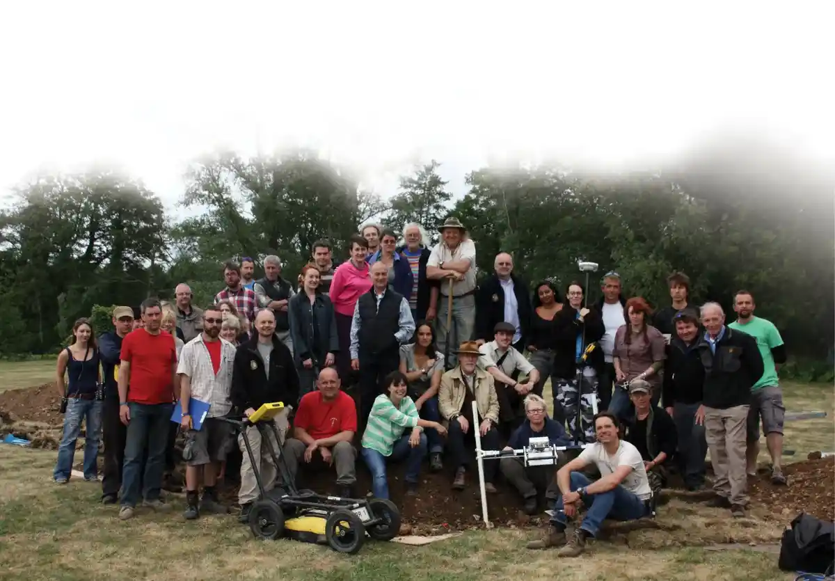 a large group of people, mostly men and women in casual outdoor clothing, pose for a group photo in a grassy field with…