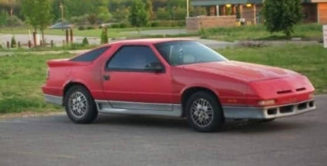 a red 1987 dodge viper is parked on a paved surface with grass and trees in the background. the car has a distinctive…