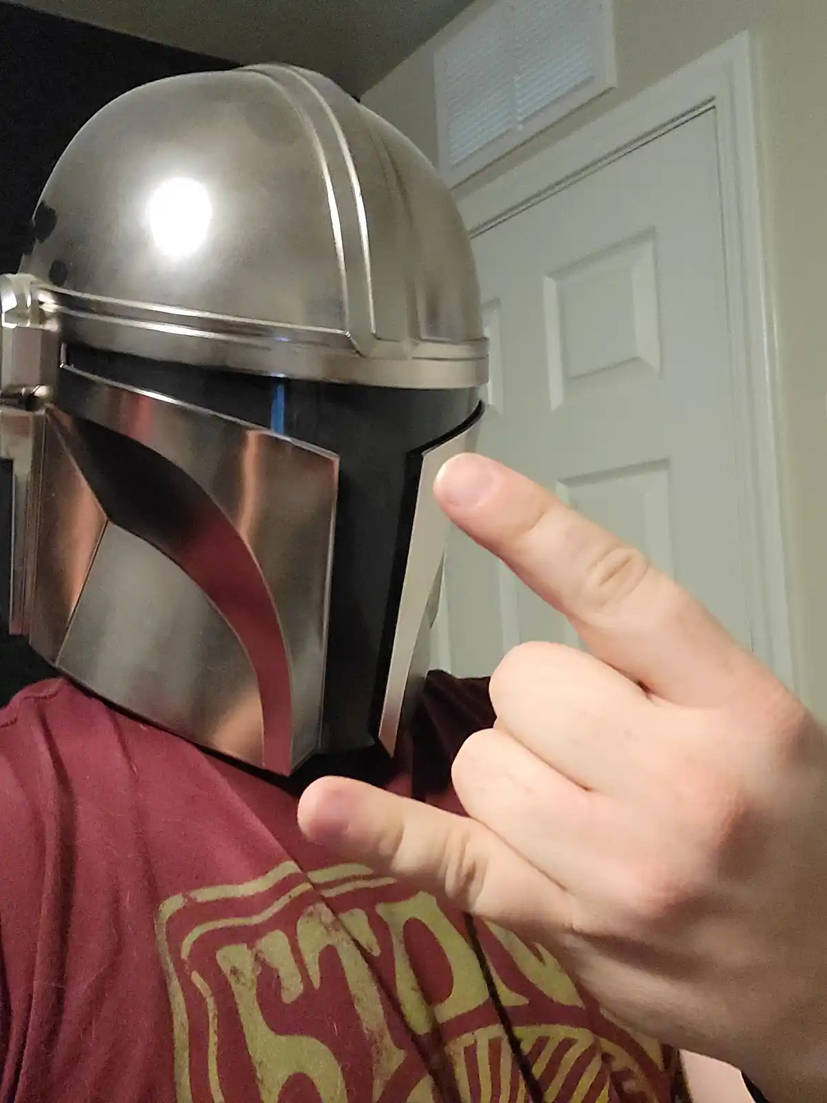 A person wearing a Mandalorian helmet from Star Wars points at the side of their own helmet with their index finger while…