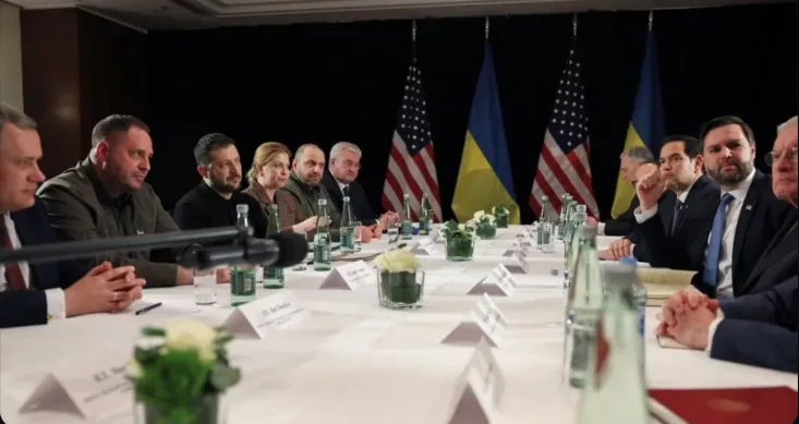 A formal meeting scene with multiple world leaders seated at a long table with name cards, water bottles, and floral…