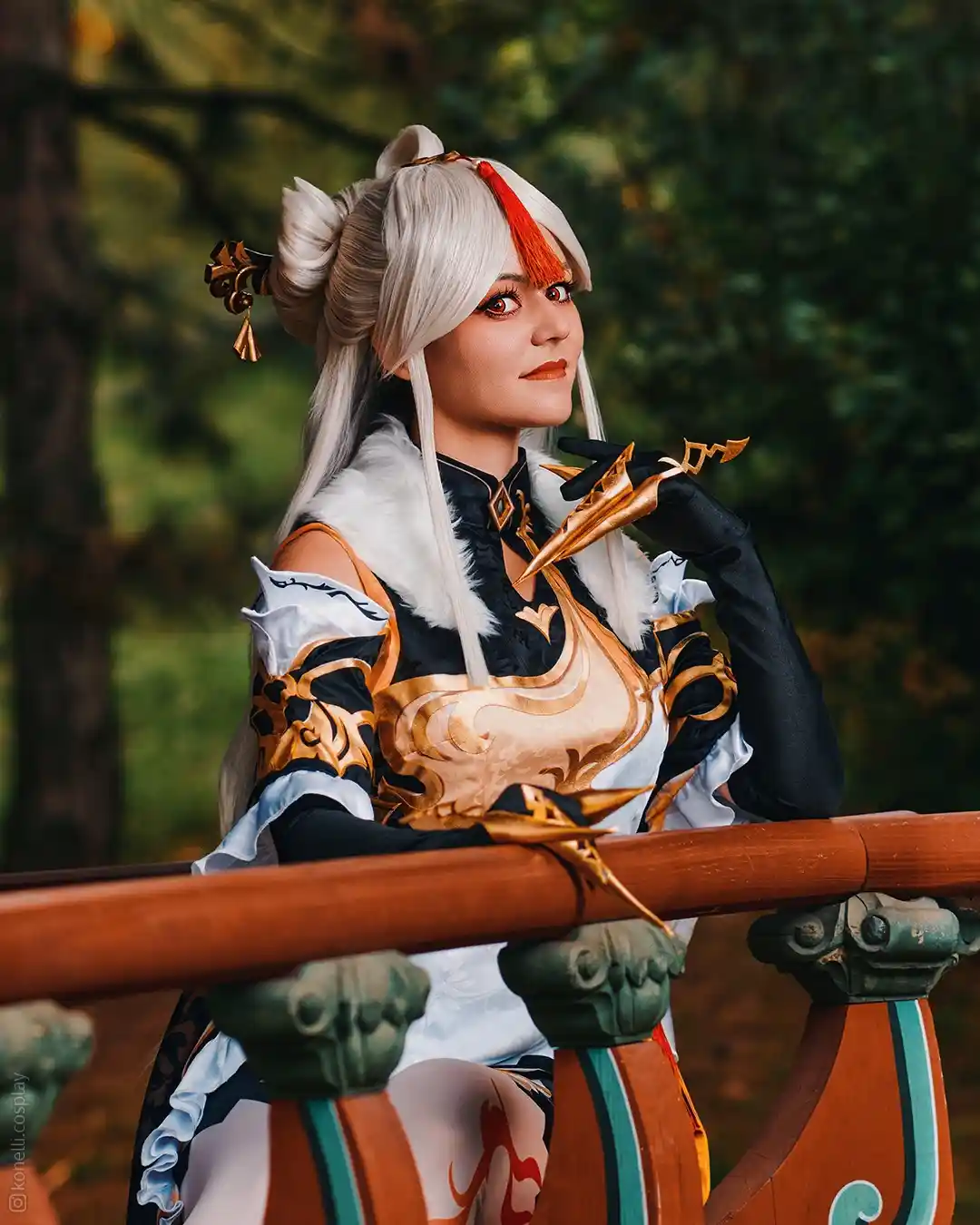 A person in a detailed cosplay of a character with white hair, red eyes, and ornate black and gold clothing sits on a wooden…