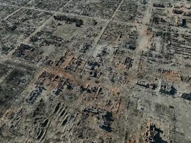 An aerial photograph shows a town completely destroyed by fire, with only charred rubble and skeletal remains of buildings…