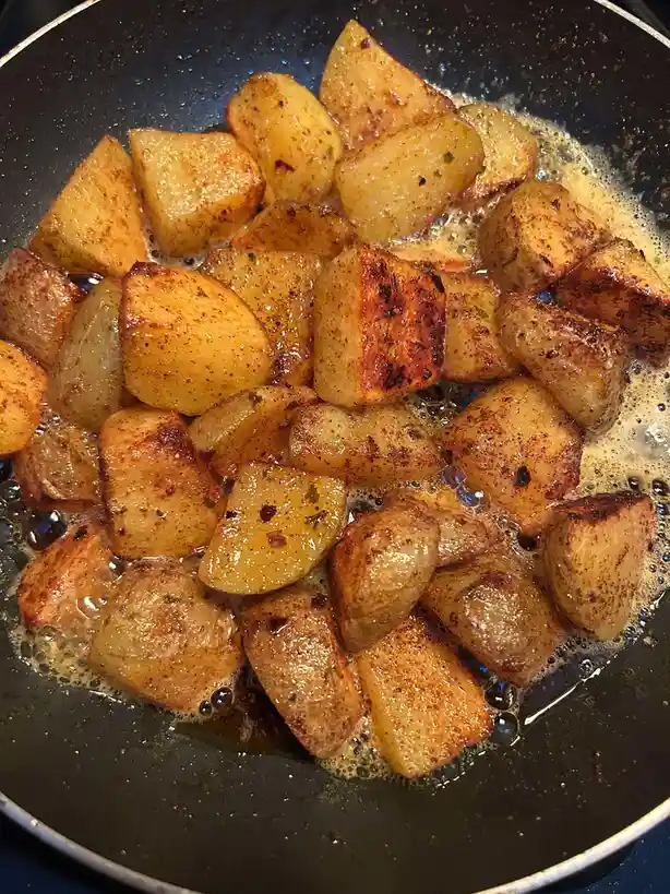 A close-up photo shows golden-brown, cubed potatoes frying in a black skillet with bubbling oil and seasoning. Overlaid text…