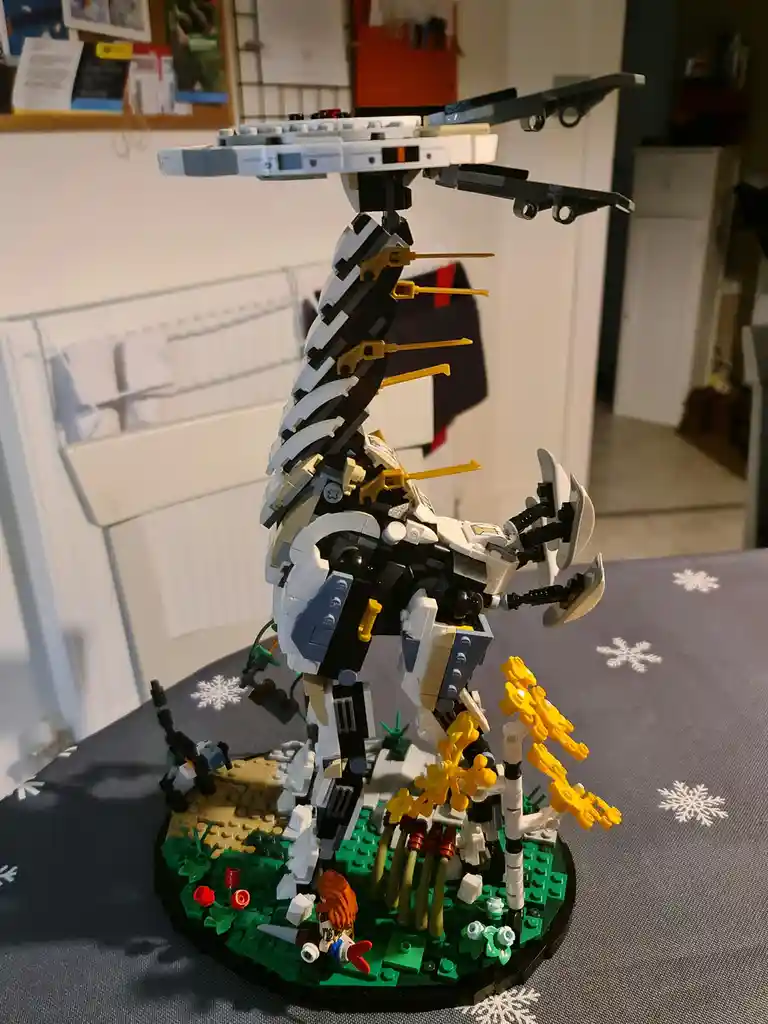 A LEGO model of a large, complex, and oddly posed mechanical creature stands on a circular base with green and tan terrain…