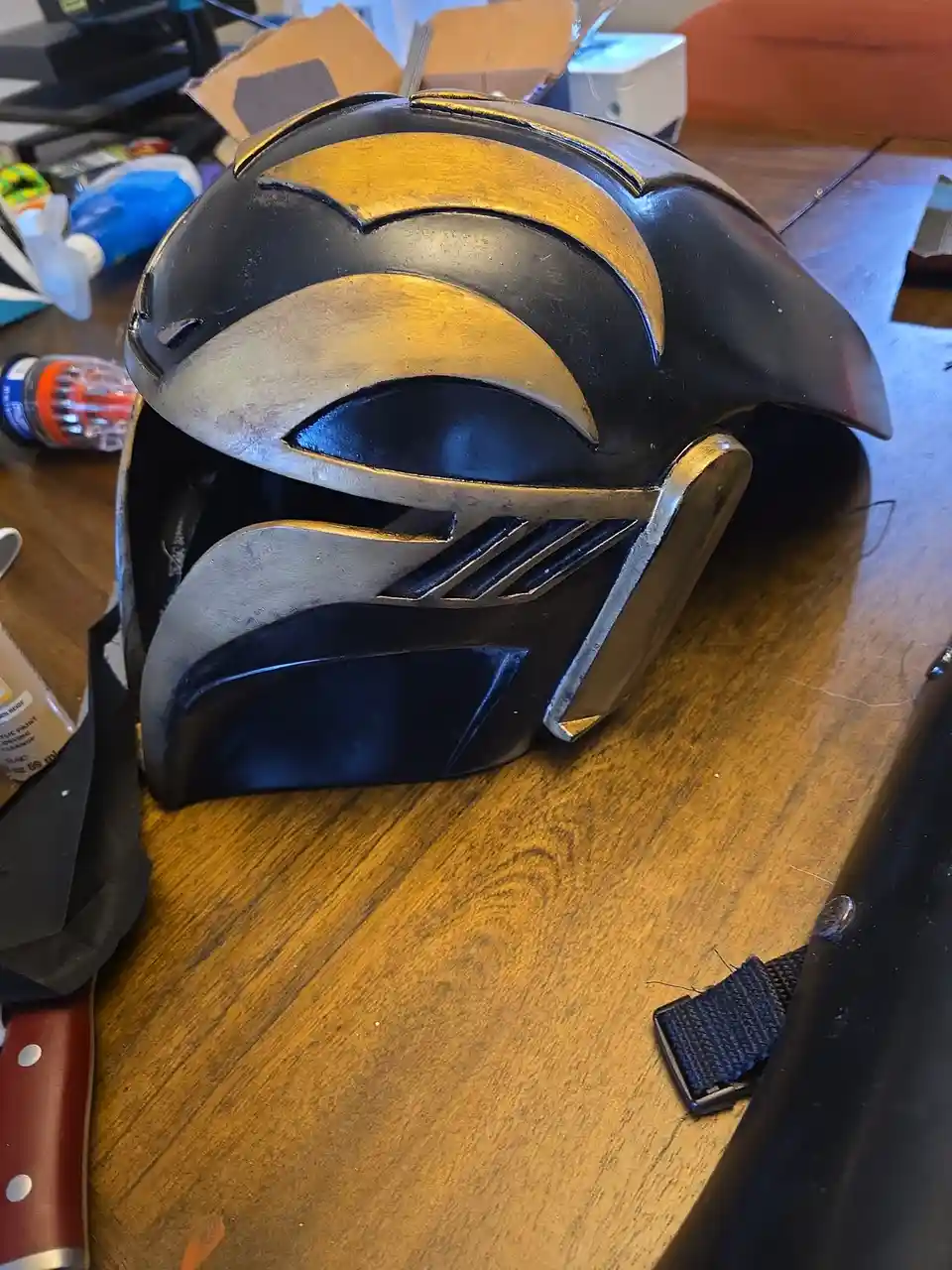 A handmade black and gold helmet, resembling a sci-fi or fantasy design with angular features and a visor, sits on a…