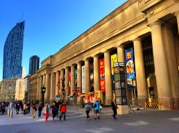 A wide-angle photo of the grand, classical facade of the New York Public Library, featuring its iconic stone columns and…