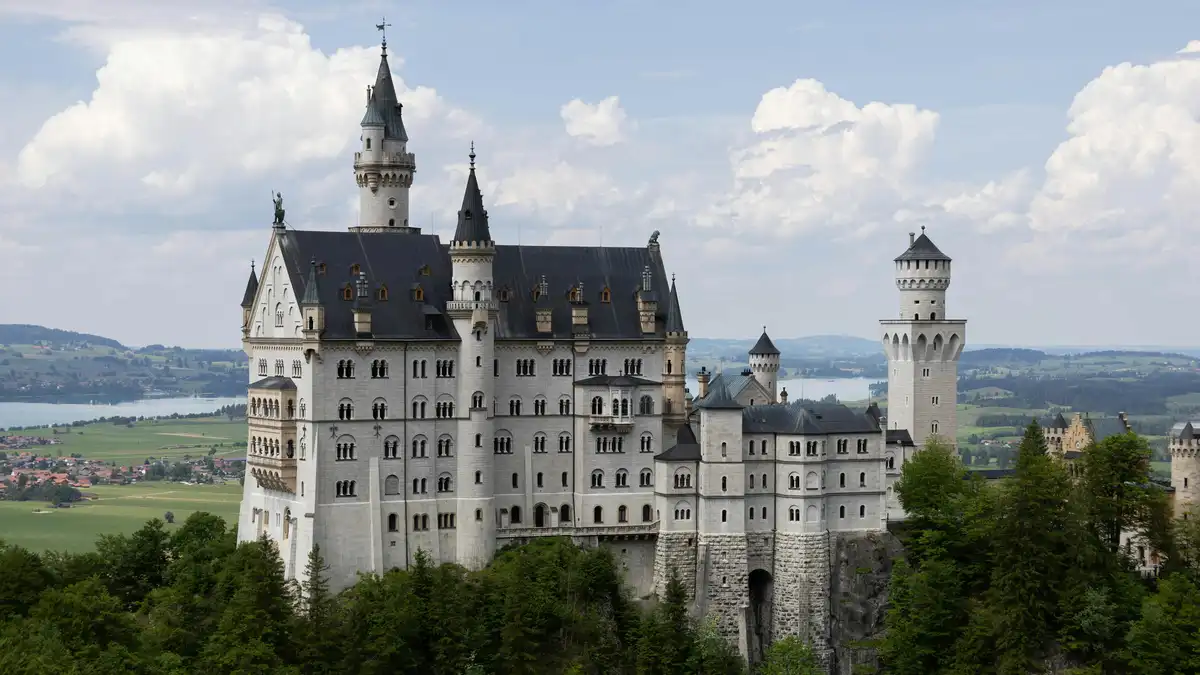 Turrets and towers rise from the misty foothills, Neuschwanstein Castle's turrets and battlements a shimmering lacework…