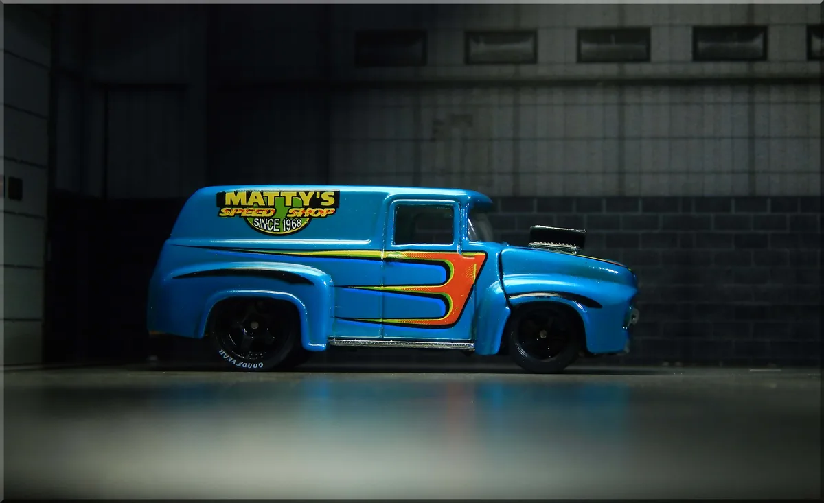 A blue die-cast model of a vintage hot rod van with 'MATTY'S SPEED SHOP SINCE 1968' decal on the side, featuring orange and…