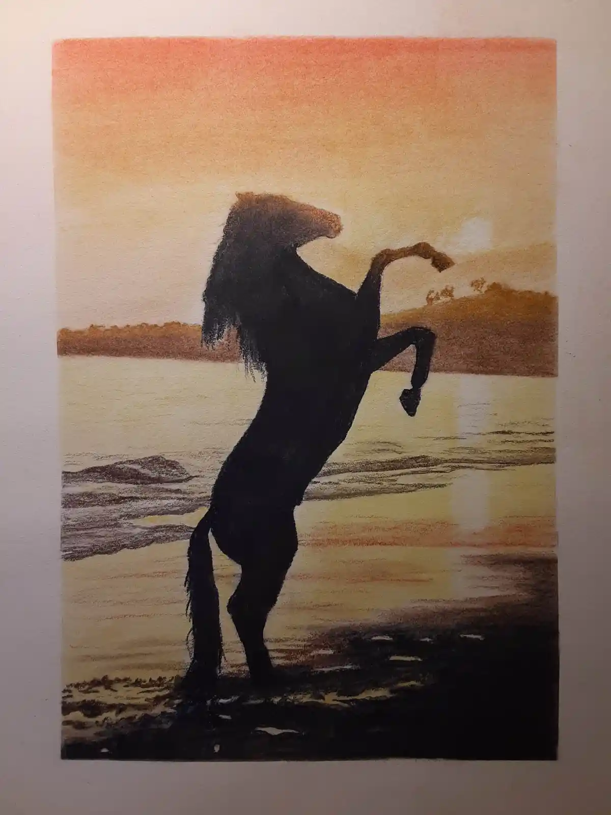 A pastel drawing depicts a black horse rearing up on its hind legs at a shoreline during sunset, with warm orange and yellow…