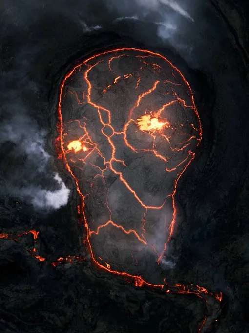 an aerial view of a volcanic crater where glowing orange lava flows form the distinct shape of a human head, with fissures…