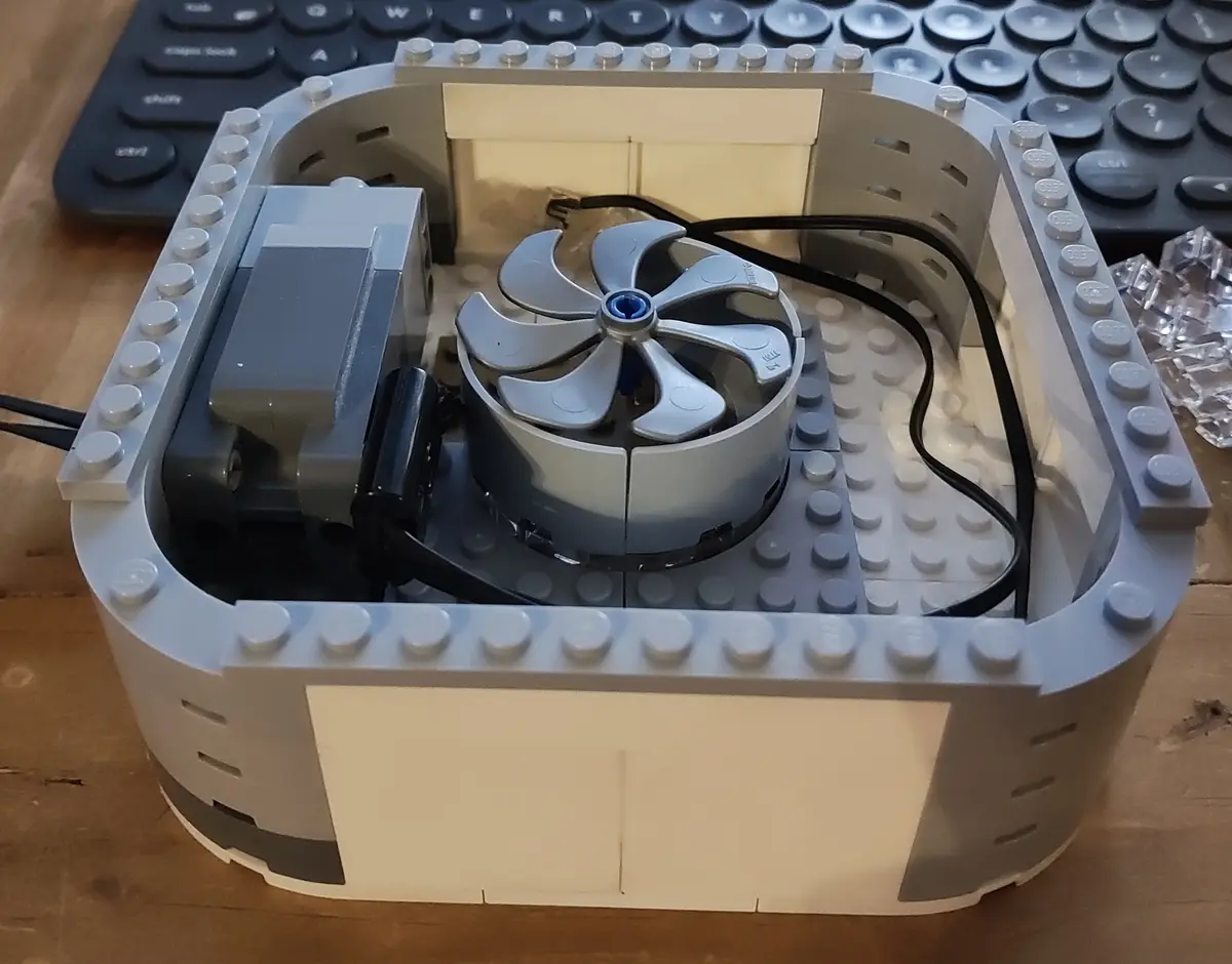 A close-up photo shows a custom-built computer case constructed entirely from gray and white LEGO bricks, with a visible…