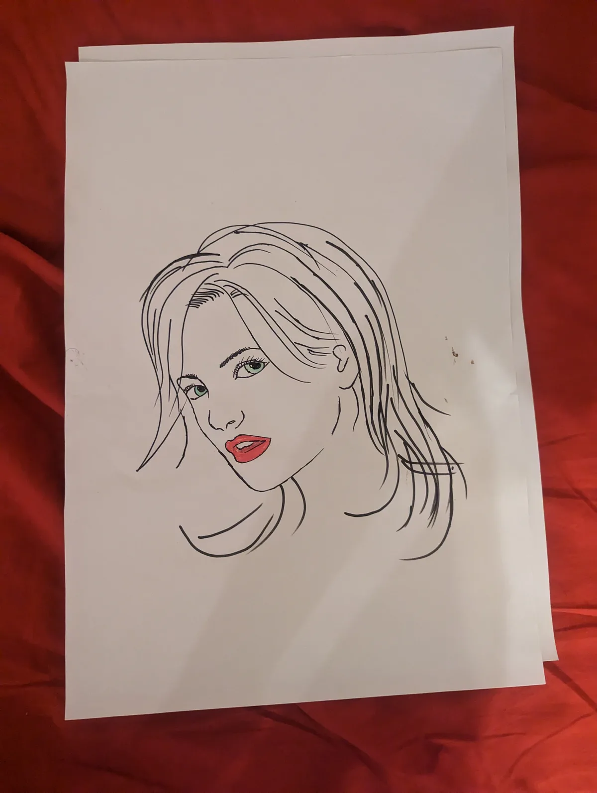 A hand-drawn portrait on white paper shows a woman with long hair, green eyes, and red lips, set against a red fabric…