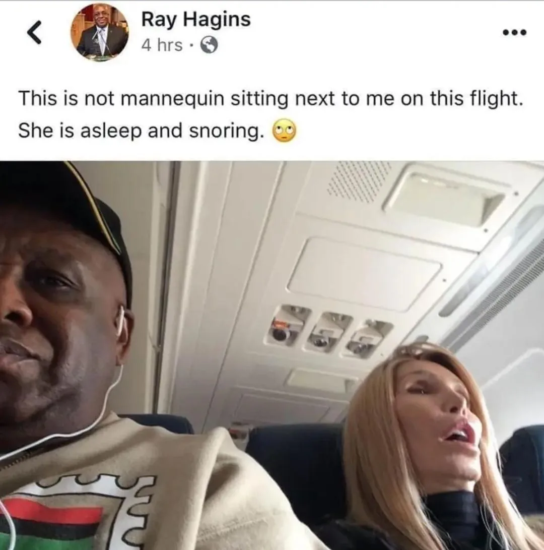 A man in a cap and hoodie with earbuds sits on an airplane, looking toward the camera. Next to him, a woman with blonde hair…