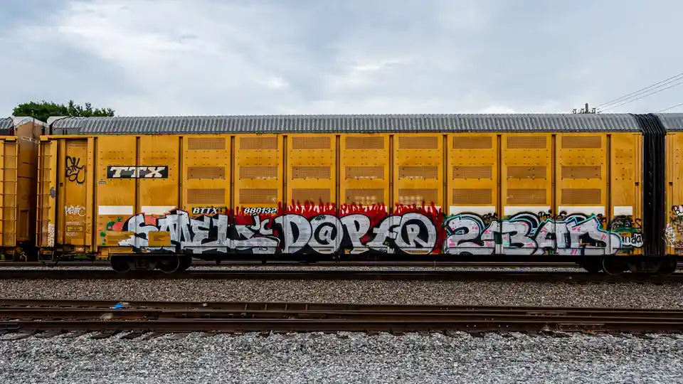 A yellow freight train car covered in graffiti, with the text 'swedish dopa 2141' prominently displayed in stylized…