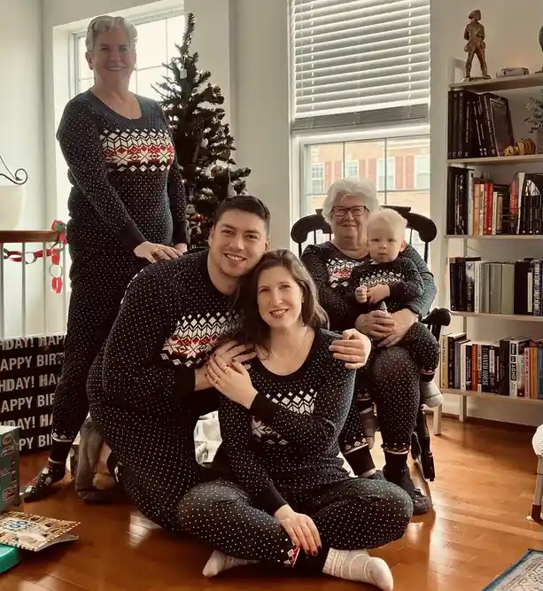 A family of five poses together in matching black pajamas with white polka dots and red/white geometric patterns, in a…