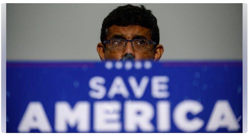 A man with dark hair and glasses peers over a blue banner that reads 'SAVE AMERICA' in large white letters. His face is…