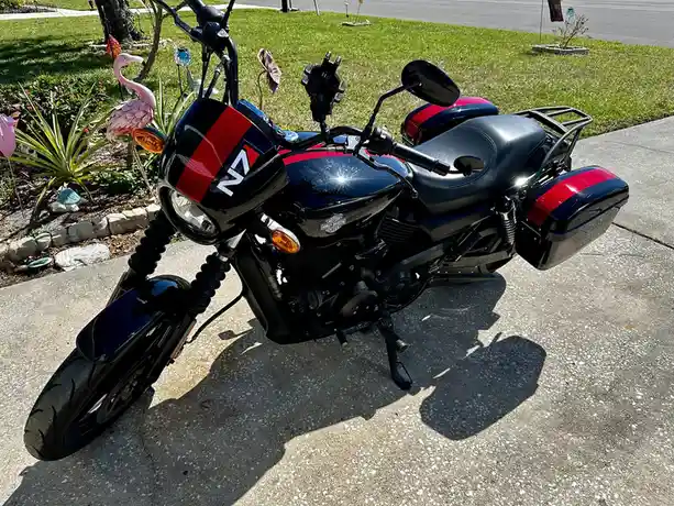 A black and red Harley-Davidson motorcycle is parked on a concrete driveway, with a pink flamingo garden ornament visible in…
