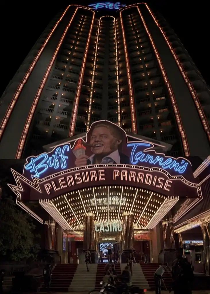 A nighttime shot of a towering, brightly lit casino building with neon signs. The main entrance features a large marquee…