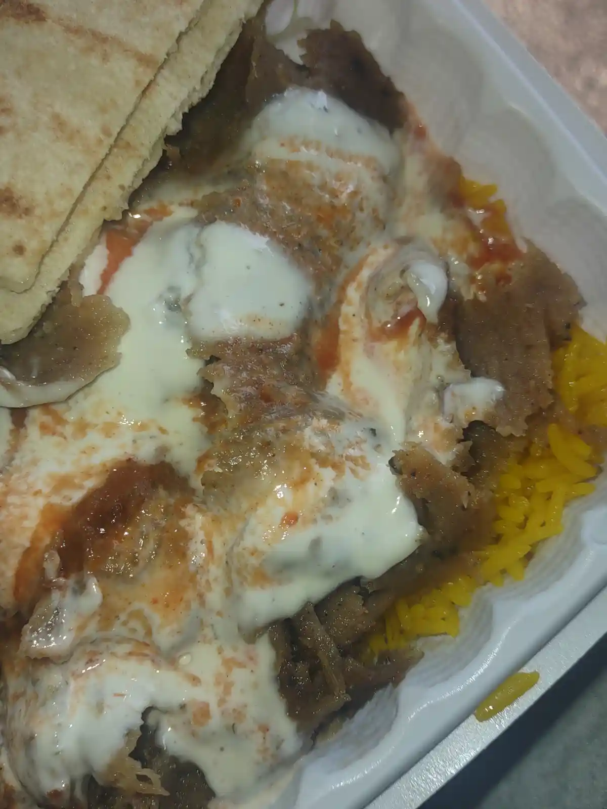 A close-up photo of a takeout container filled with shredded meat, yellow rice, and a folded flatbread, all generously…