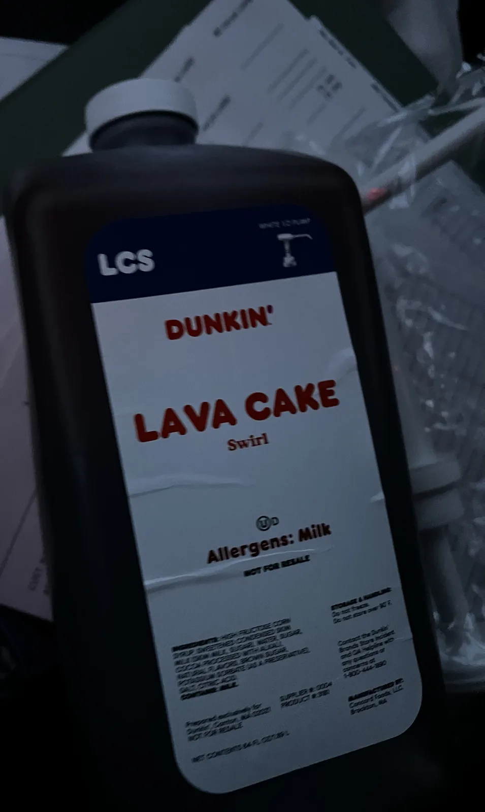 A close-up of a black plastic bottle labeled 'DUNKIN' LAVA CAKE Swirl' with 'LCS' and 'NOT FOR RETAIL' printed on it. The…