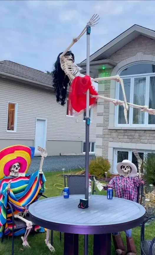 Three skeleton decorations are set up in a backyard for a party. One skeleton is hanging upside down from a tall patio pole…