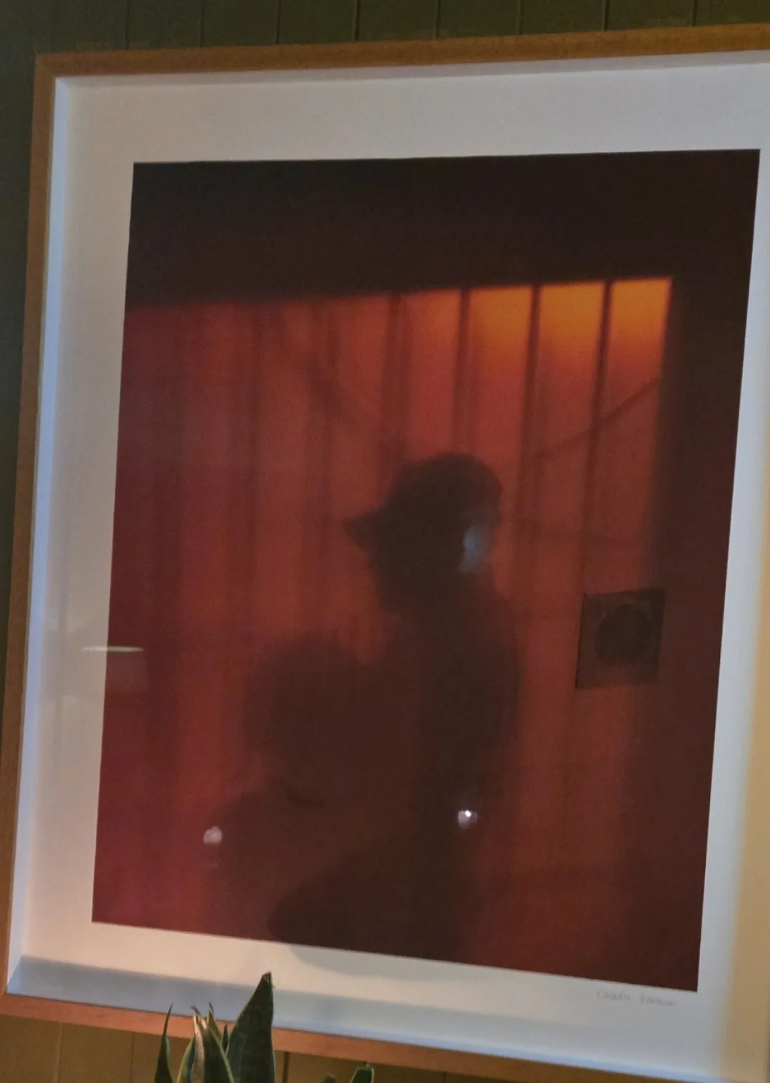 A framed photograph shows a blurry, reddish-orange silhouette of a person wearing a cap, seemingly holding a small object…