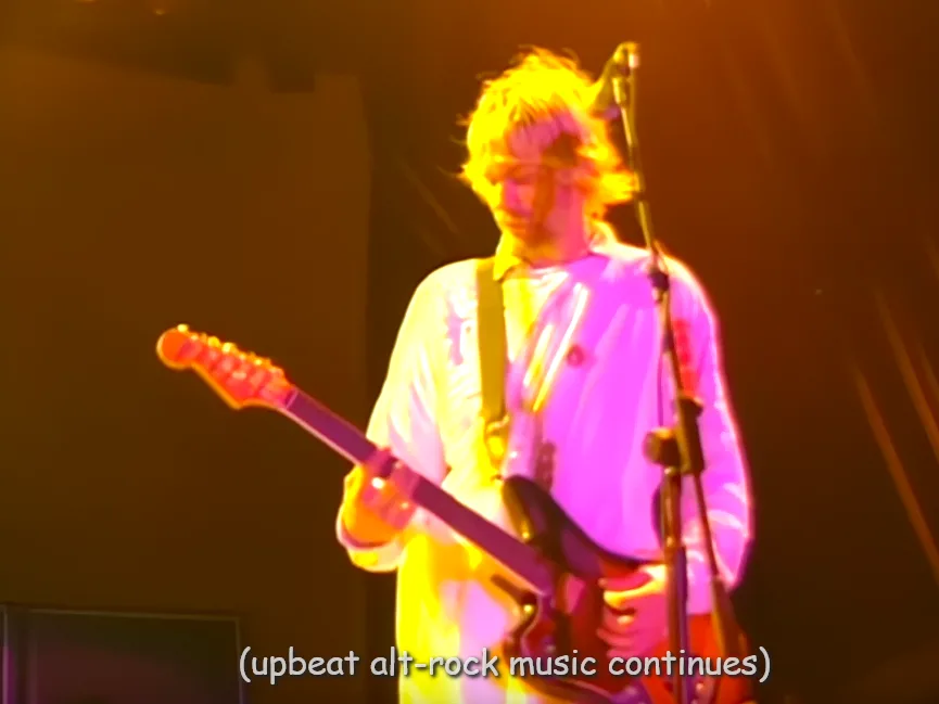 A musician with blonde hair, wearing a white shirt and holding an electric guitar, is shown on stage under intense orange…