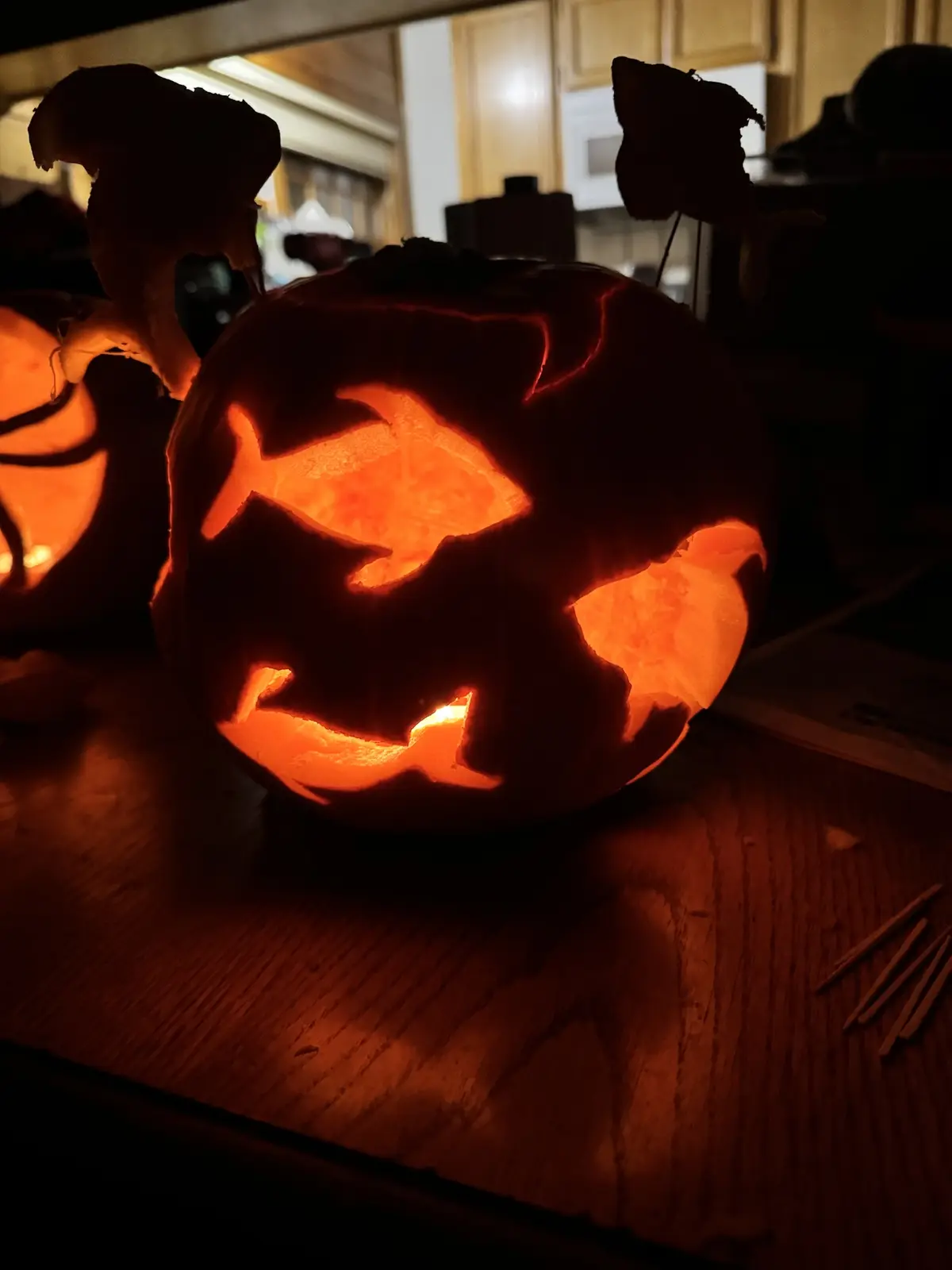 A close-up of a carved Halloween pumpkin glowing from within, its face shaped like a fish with triangular eyes and a jagged…