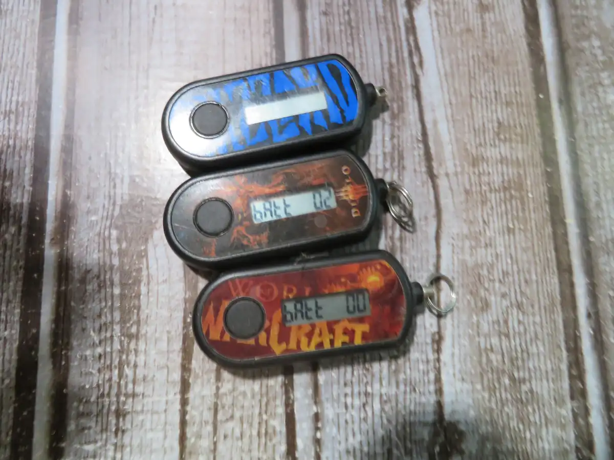 Three small, oval-shaped electronic devices with keyrings lie on a wooden surface. The top one has a blue and black design…
