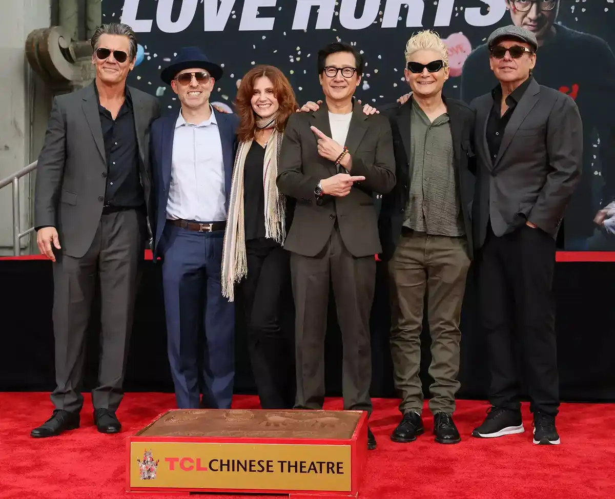 Six actors pose together on a red carpet at the TCL Chinese Theatre, standing behind a handprint slab. The backdrop features…