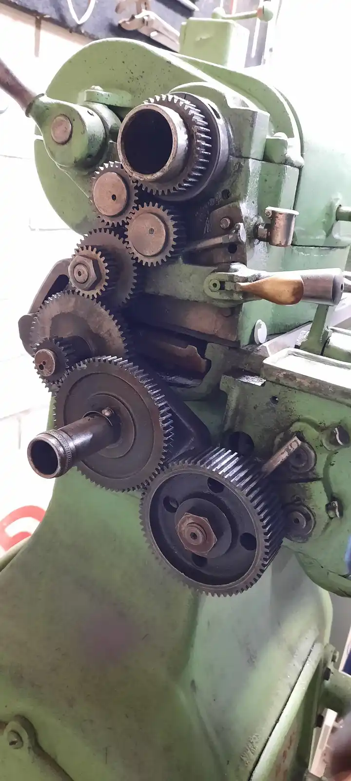 A close-up of a green, rusty industrial machine with multiple interlocking metal gears and shafts, showing signs of wear and…