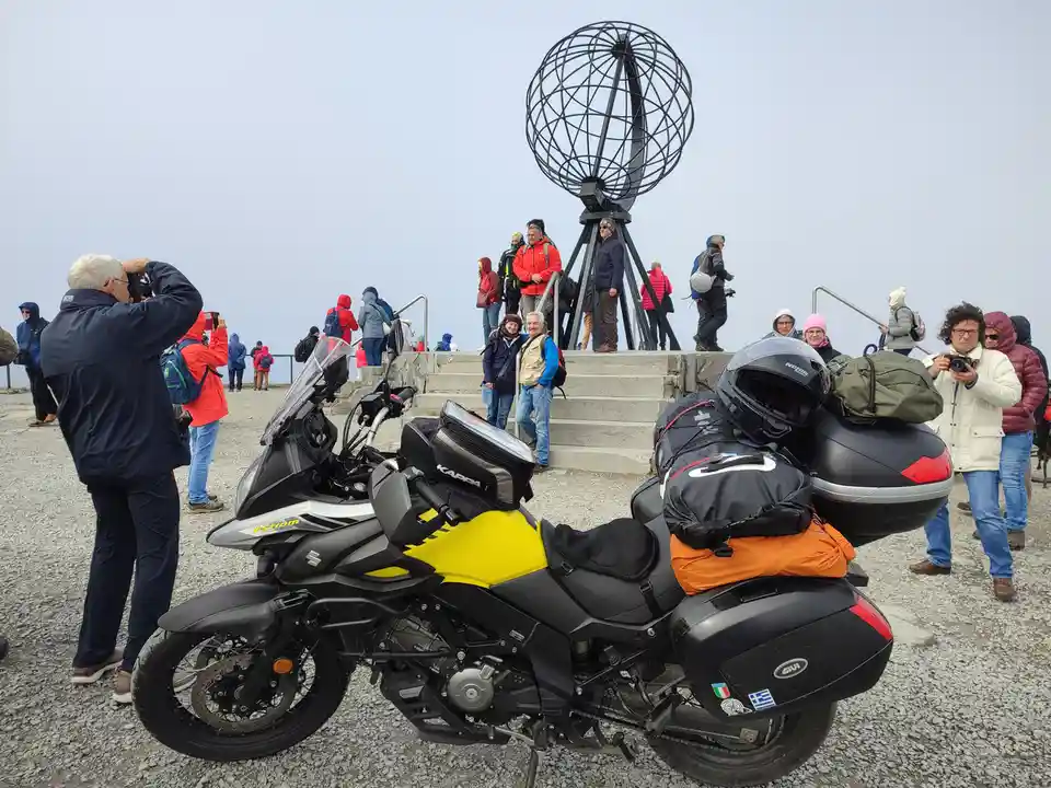 A heavily loaded touring motorcycle with yellow and black paint, equipped with saddlebags, a top case, and a helmet, is…