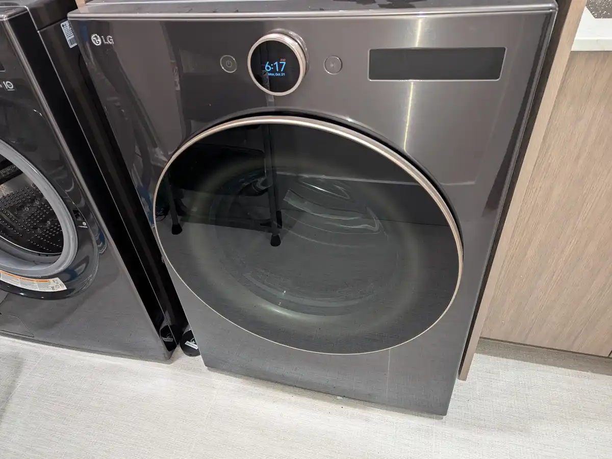 A close-up of a modern, dark gray LG front-loading washing machine in a retail setting, its digital display showing the time…