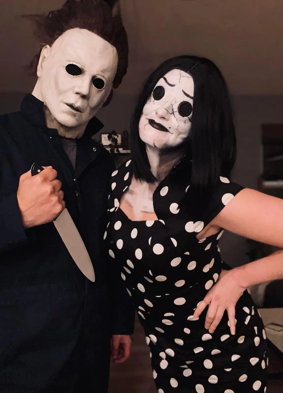 Two people in Halloween costumes pose for a photo: one as Michael Myers holding a knife, the other as a character with a…