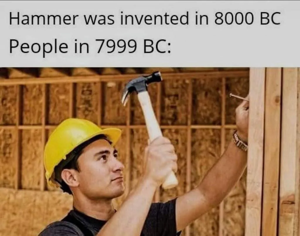 A man wearing a yellow hard hat and a dark t-shirt is shown hammering a nail into a wooden frame. He holds a claw hammer…