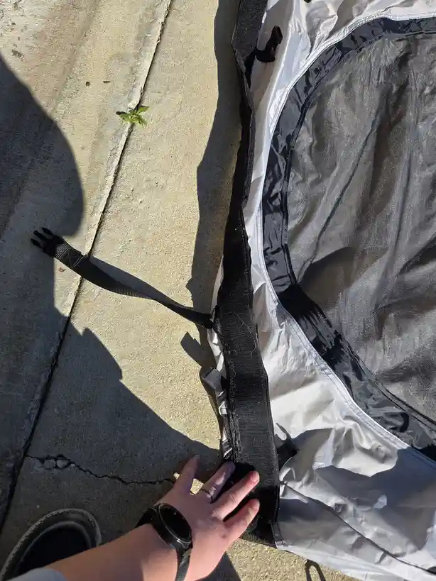 A person's hand touches the edge of a partially unrolled black and white tent lying on a concrete sidewalk, with a small…