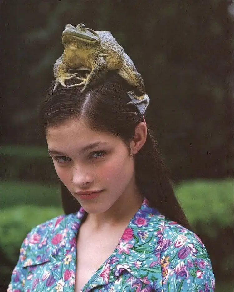 A young woman with dark hair and a floral-patterned shirt looks directly at the camera with a calm expression while a large…