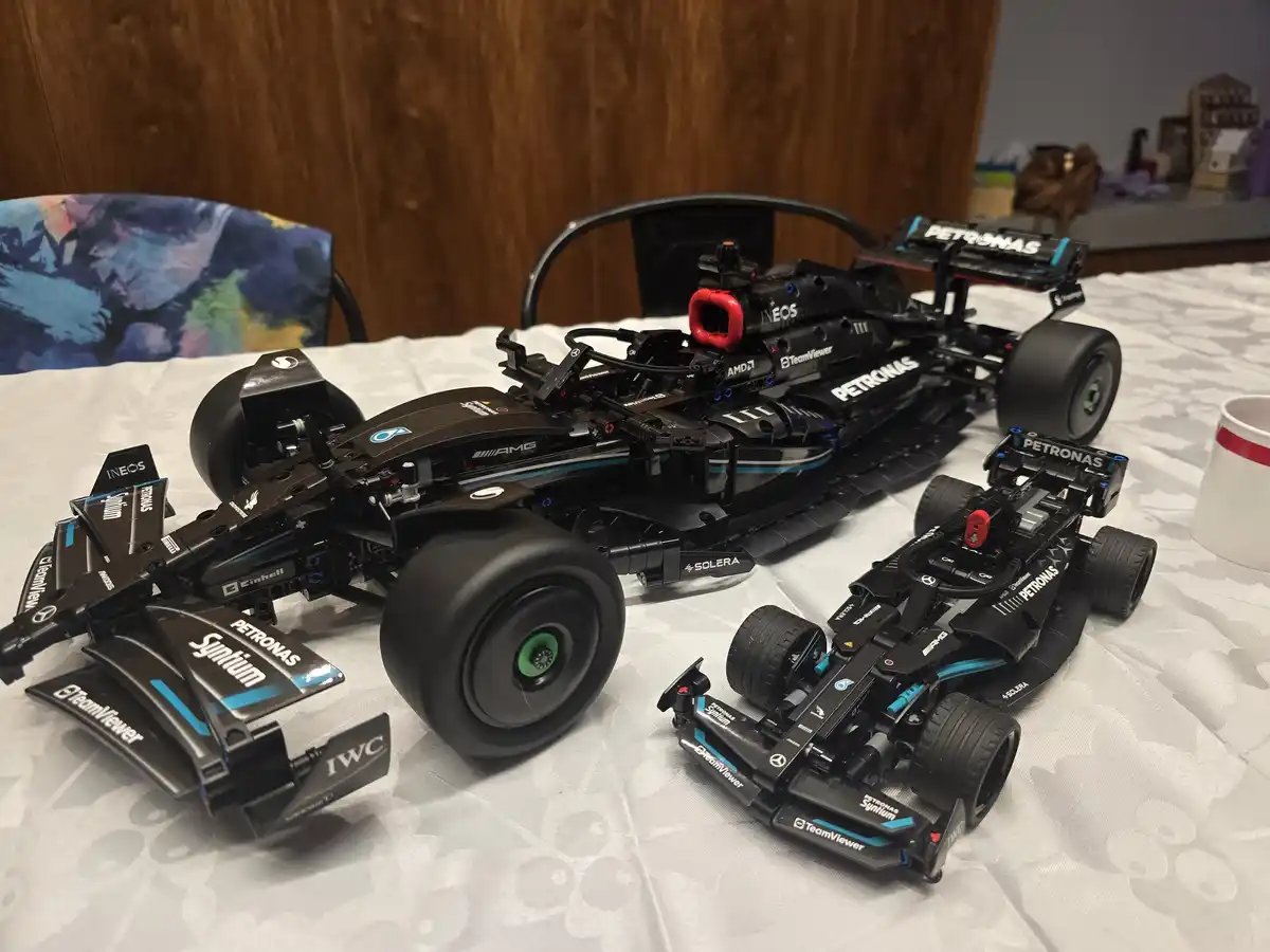 Two detailed black Lego Formula 1 car models, one large and one small, sit on a white patterned tablecloth. Both feature…