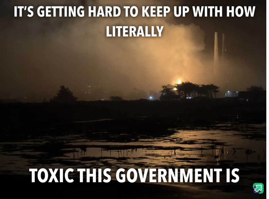 A nighttime photo shows a factory with smokestacks emitting thick, orange-tinged smoke into the sky, reflecting on a wet…
