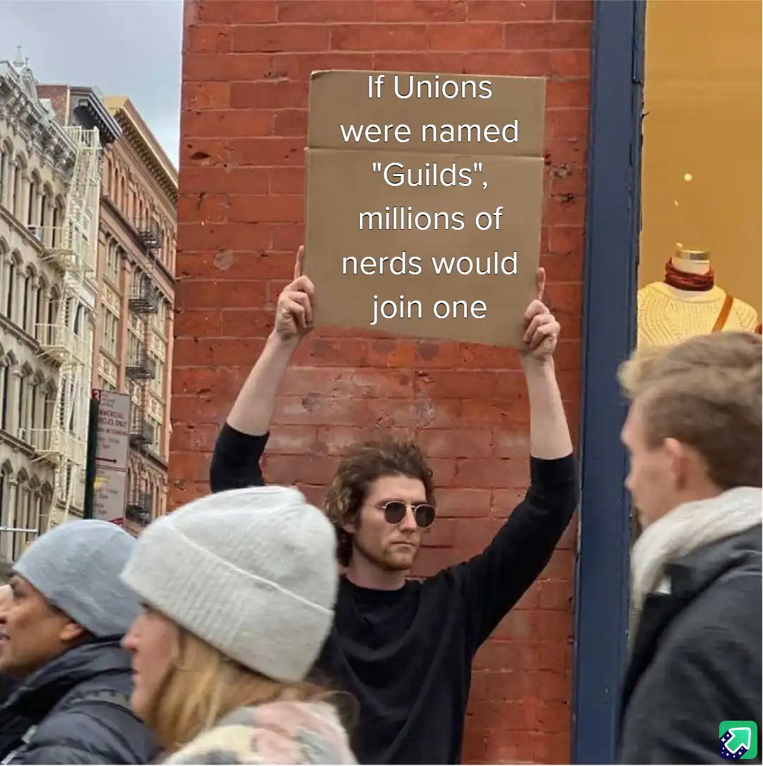 A person with curly hair and sunglasses holds up a cardboard sign in a city street with brick buildings and pedestrians…