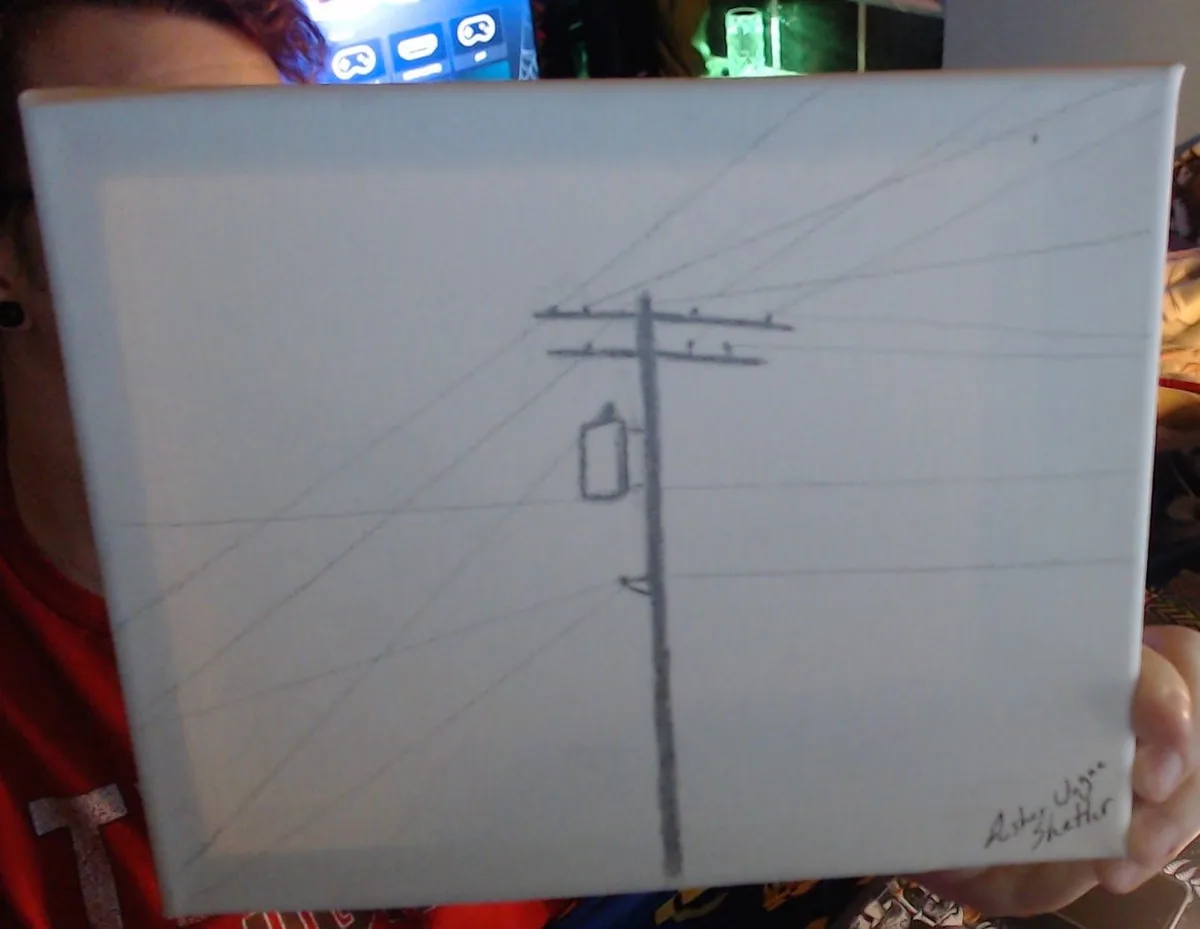 A person holds up a white canvas with a simple pencil drawing of a utility pole with wires and a transformer box. The…