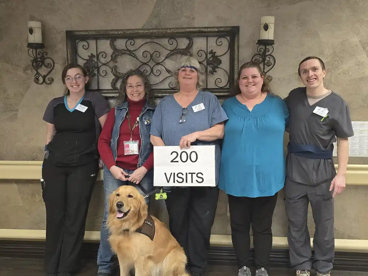 Five smiling staff members and a golden retriever pose for a photo in what appears to be a healthcare facility lobby. One…