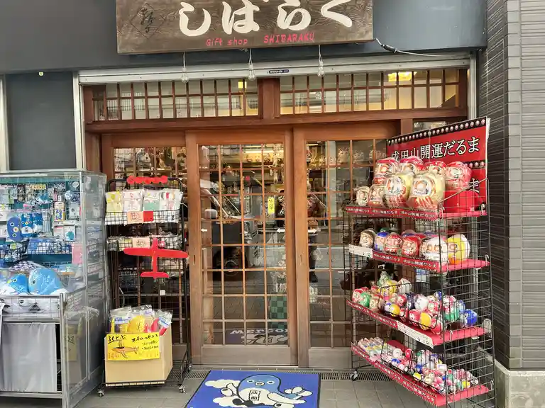 A storefront of a Japanese gift shop named 'Shibaraku' with wooden doors and traditional architecture, displaying racks of…