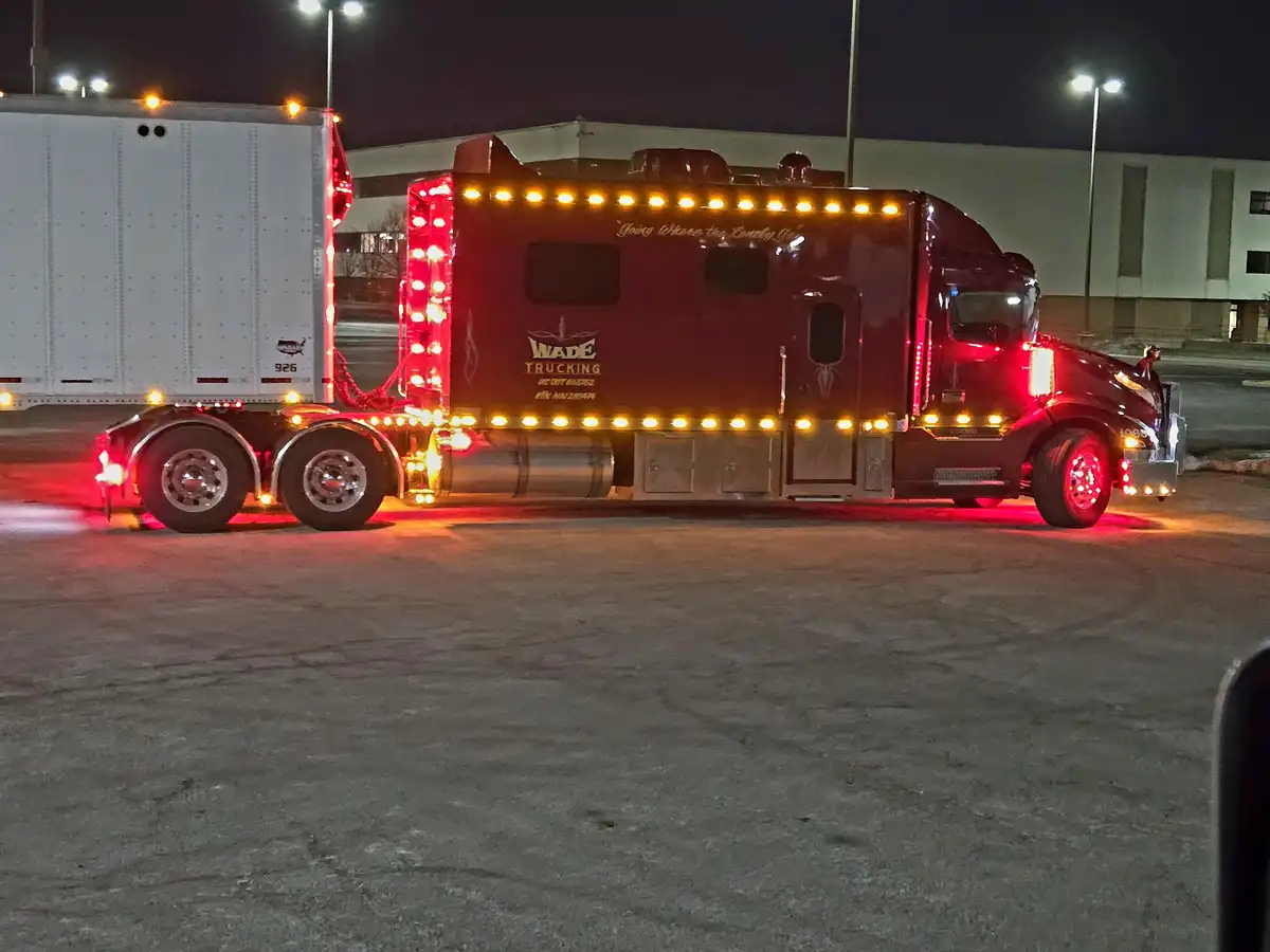 A red semi-truck with a custom 'Wade Trucking' logo and the slogan 'Going Where the Lonely Go' is parked at night…